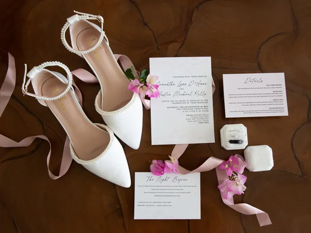 A wedding invitation suite, rings and bridal shoes arranged on a wood table